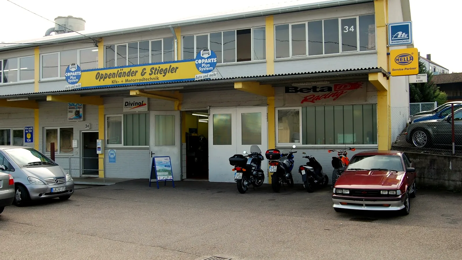 Außenansicht des Betriebs Oppenländer & Stiegler mit Firmenschild und Motorrädern davor