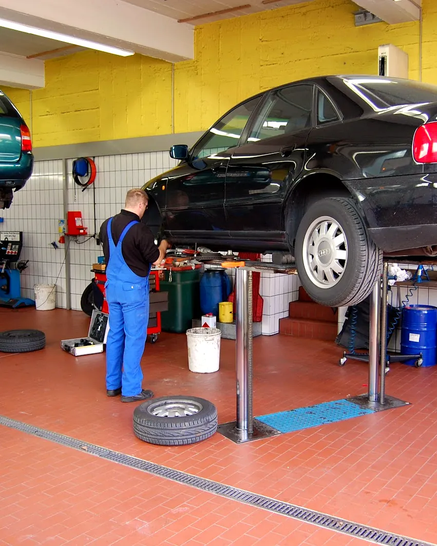 Monteur in blauem Arbeitsanzug arbeitet an einem angehobenen Auto in der Werkstatt von Oppenländer & Stiegler